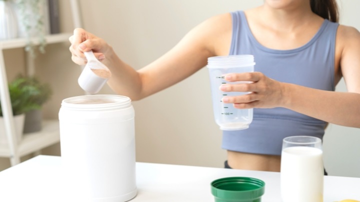 woman putting a scoop of protein powder in her shaker bottle
