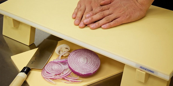 persons hands on a soft cutting board and a knife and a onion under it 